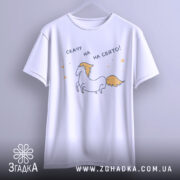 Футболка скачу на свято, біла, підвішена на вішалці, фон світло-сірий, принт з єдинорогом та текстом 'скачу на свято!', вигляд спереду.