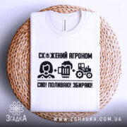 Футболка скажений агроном, біла, складена на плетеній основі, фон нейтральний, принт чорного кольору з текстом і іконками, що зображують агронома, пиво та трактор.