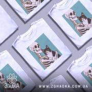 Футболка скелет кіт білого кольору, зображена з фронтального ракурсу на манекені, фон світло-сірий, принт зображає скелет, що тримає чорного кота з великими очима.