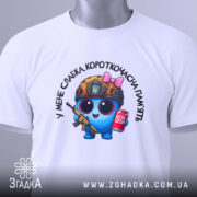 Футболка слабка пам`ять, біла, складена на поверхні з верхнього ракурсу, фон світлий, принт з персонажем у військовій касці, з автоматом та банкою напою, на комірці є етикетка.