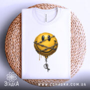 Футболка смайл у колючках, біла, складена на кошику, фон світло-сірий, принт з жовтим смайлом у колючках, з краплями фарби.