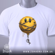 Футболка смайл у колючках, біла, складена на столі, фон світло-сірий, принт з жовтим смайлом у колючках, з етикеткою зеленого кольору.
