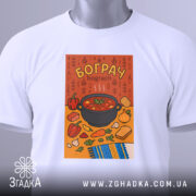 Футболка смак бограчу, біла, зображена на столі, фон світло-сірий, принт з каструлею бограчу та овочами на помаранчевому фоні, з етикеткою на комірці, деталі принта чіткі та яскраві.