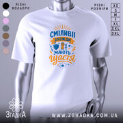 Футболка сміливі мають щастя, білого кольору, зображена з правого ракурсу на манекені, фон світло-сірий, принт містить яскраві кольори: синій і оранжевий, з написом та ілюстраціями, що символізують сміливість.