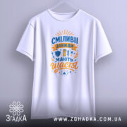 Футболка сміливі мають щастя, білого кольору, підвішена на вішалці, фон світло-сірий, принт яскравий, з елементами, що символізують сміливість, напис великими літерами.