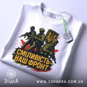 Футболка сміливість наш фронт, біла, складена на поверхні, фон світло-сірий, принт з трьома солдатами та гербом України, прикріплена етикетка, кольори принта чорний, жовтий, червоний.