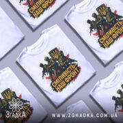 Футболка сміливість наш фронт, біла, зображена на манекені, фон світло-сірий, принт з трьома солдатами та гербом України, кольори принта чорний, жовтий, червоний.