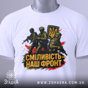 Футболка сміливість наш фронт, біла, складена на поверхні, фон світло-сірий, принт з трьома солдатами та гербом України, прикріплена етикетка, кольори принта чорний, жовтий, червоний.