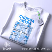 Футболка сніжна битва, біла, лежить на поверхні, фон світлий, принт з чотирма сніговиками, що виконують різні дії, текст синій, на комірці є етикетка з зеленим шнурком.