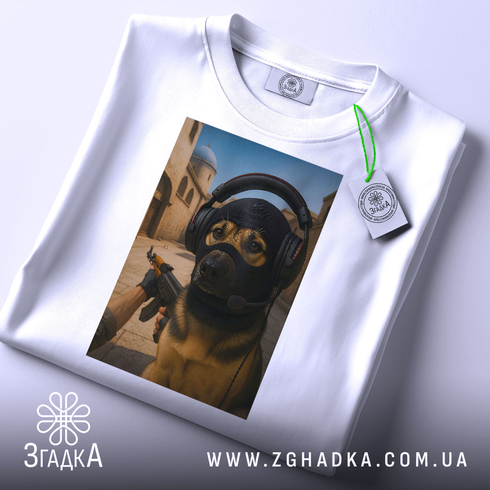 Футболка собака геймер, біла, зображена на столі, фон світлий, принт з собакою в навушниках та масці, на фоні ігрового середовища, з етикеткою на рукаві.