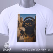 Футболка собака геймер, біла, зображена на столі, фон світлий, принт з собакою в навушниках та масці, на фоні ігрового середовища, з етикеткою на рукаві.