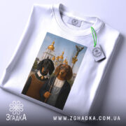 Футболка собаки мистецтво Києва, біла, зображена на столі, ракурс зверху, фон світлий, принт з двома собаками в одязі на фоні архітектури з золотими куполами, з етикеткою.