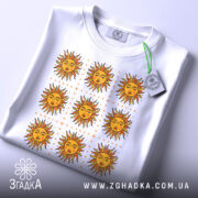 Футболка сонячна енергія, біла, зображена на столі, фон світлий, принт з дев'яти сонць з червоними променями та жовтими обличчями, на футболці є зелений етикет.