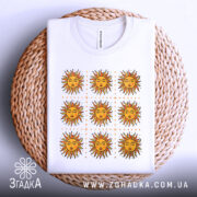 Футболка сонячна енергія, біла, зображена на кошику, фон світлий, принт з дев'яти сонць з червоними променями та жовтими обличчями, футболка акуратно складена.