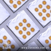 Футболка сонячна енергія, біла, зображена на манекені, фон сірий, принт складається з дев'яти сонць з червоними променями та жовтими обличчями, розташованих у три ряди по три.