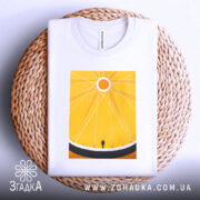 Футболка сонячне колесо. Біла футболка, складена на плетеному кошику, з жовтим принтом, що зображає сонце та фігуру людини. Ракурс зверху, фон світло-сірий, деталі принта яскраві.