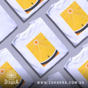 Футболка сонячне колесо. Біла футболка з яскравим жовтим принтом, на якому зображено сонце та лінії, що символізують промені. Ракурс зліва, фон світло-сірий, деталі принта чіткі та контрастні.