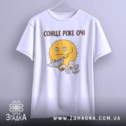 Футболка сонце ріже очі. Біла футболка на вішалці з принтом жовтого сонця, яке тримає ніж. Принт розташований на грудях, фон світло-сірий.