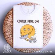 Футболка сонце ріже очі. Біла футболка, складена на плетеній основі, з принтом жовтого сонця, яке тримає ніж. Принт розташований на грудях, фон світло-сірий.