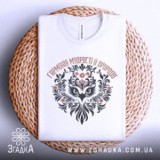 Футболка сова гармонія, біла, складена на плетеній кошику, фон білий, принт з совою та рослинними елементами в чорному і коричневому кольорах.