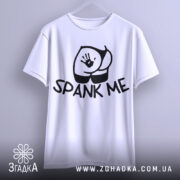 Футболка спанк-арт білого кольору, підвішена на вішалці, фон світло-сірий, принт з чорним малюнком сідниць та написом 'SPANK ME', видно округлість рукавів.