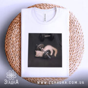 Футболка спорт котик, біла, складена на плетеному кошику, фон світло-сірий, принт з котиком, що грає з гантелями на чорному фоні.