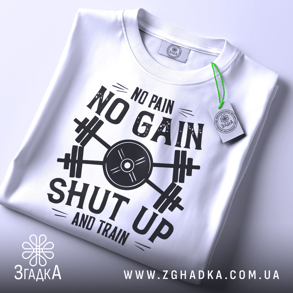 Футболка спортивний дух, біла, складена на поверхні, фон світло-сірий, принт чорного кольору з написом 'NO PAIN NO GAIN SHUT UP AND TRAIN' та етикетка з зеленим шнурком.