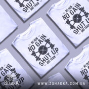 Футболка спортивний дух, біла, зображена на манекені з правого боку, фон світло-сірий, принт чорного кольору з написом 'NO PAIN NO GAIN SHUT UP AND TRAIN' та зображенням гантель.