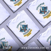 Футболка справжній чоловік, біла, зображена з фронтального ракурсу, на фоні світло-сірого кольору, принт з двома сокирами та горами, текст українською мовою.