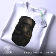 Футболка сталкер атмосфера, біла футболка з принтом, ракурс зверху, фон світло-сірий, деталі принта зображують персонажа в протигазі, на футболці є етикетка з логотипом.