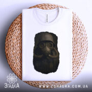 Футболка сталкер атмосфера, біла футболка з принтом, ракурс зверху, фон світло-сірий, деталі принта зображують персонажа в протигазі, футболка лежить на плетеній основі.