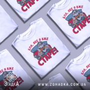 Футболка старе скелет, біла, зображена на манекені, фон світло-сірий, принт з черепом за кермом автомобіля, текст червоним кольором 'Бля, яке я вже СТАРЕ!'.