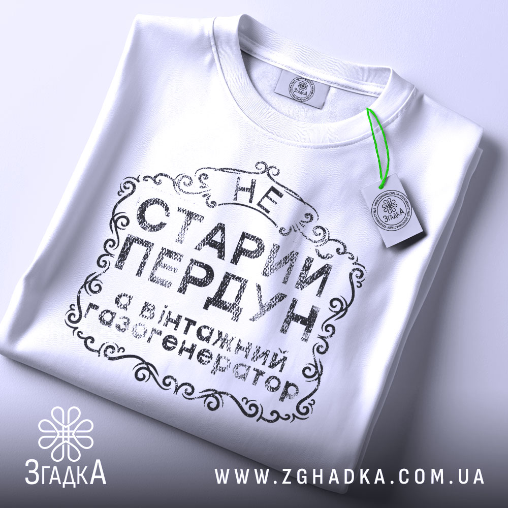 Футболка старий пердун, біла, складена на поверхні, фон світлий, принт чорного кольору з декоративними елементами, на ярлику зелена стрічка.