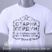 Футболка старий пердун, біла, складена на поверхні, фон світлий, принт чорного кольору з декоративними елементами, на ярлику зелена стрічка.