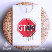 Футболка стоп старт арт, біла, складена на кошику, фон світлий, принт червоного кольору у формі знака стоп з написом 'START' чорним кольором, з елементами графіті.