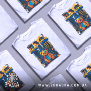 Футболка стоп війна, біла, зображена на манекені, фон нейтральний, принт з ведмедиком у кольоровій палітрі на фоні зруйнованого міста.