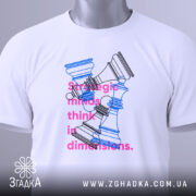 Футболка стратегічні шахи білого кольору, складена на поверхні, фон світло-сірий, принт з шаховими фігурами в блакитному та рожевому кольорах, текст на футболці читається: 'strategic minds think in dimensions.', на комірці видна етикетка.