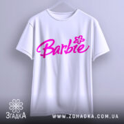 Футболка стиль барбі, біла, підвішена на вішалці, фон світло-сірий, принт з написом 'Barbie' яскравого рожевого кольору з квіткою.