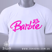 Футболка стиль барбі, біла, складена на поверхні, фон світлий, принт з написом 'Barbie' яскравого рожевого кольору, з етикеткою на комірці.