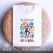 Футболка стиль Матісса, біла, складена на плетеній кошику, фон світло-сірий, принт з кольоровими квітами та фігурою людини в чорному.