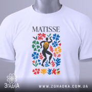 Футболка стиль Матісса, біла, складена на столі, фон світло-сірий, принт з кольоровими квітами та фігурою людини в чорному, з етикеткою.