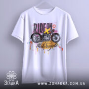 Футболка стиль мотоцикліста, біла, підвішена на вішалці, фон нейтральний, принт з мотоциклом та кольоровими краплями фарби.