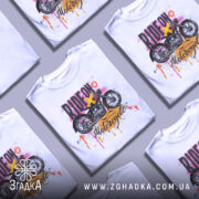 Футболка стиль мотоцикліста, біла, зображена на манекені з правого боку, фон нейтральний, принт з мотоциклом та кольоровими краплями фарби.