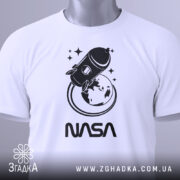 Футболка стиль NASA, біла, складена на столі, фон світло-сірий, принт з ракетою та Землею в чорному кольорі, текст 'NASA' під принтом, на футболці є етикетка.