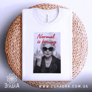 Футболка стильна бабуся, біла, з верхнього ракурсу, на фоні плетеного кошика, принт з зображенням бабусі в чорних окулярах, з червоними губами, в шкірянці, з написом 'Normal is boring' червоним шрифтом.