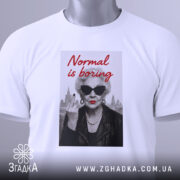 Футболка стильна бабуся, біла, з верхнього ракурсу, на фоні світло-сірого кольору, принт з зображенням бабусі в чорних окулярах, з червоними губами, в шкірянці, з написом 'Normal is boring' червоним шрифтом, з етикеткою зеленого кольору.