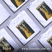 Футболка стильні коти арт, біла футболка на манекені, фон градієнт сірого кольору, принт з трьома чорними котами, один з яких у жовтій сукні, коти мають великі білі очі.