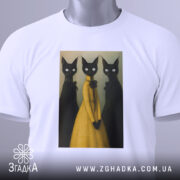 Футболка стильні коти арт, складена біла футболка на світлому фоні, принт з трьома чорними котами, один з яких у жовтій сукні, на футболці є етикетка з зеленим шнурком.