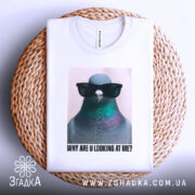 Футболка стильний голуб, біла, зображена зверху на плетеній кошику, фон світло-сірий, принт з птахом у сонцезахисних окулярах, текст під ним: 'WHY ARE U LOOKING AT ME?'.