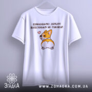 Футболка сумненькою дупцею не пукнеш. Біла футболка, підвішена на вішалці, з принтом корги, що повертається, на фоні світло-сірого градієнту. Принт зображує корги з сердечком, що виглядає весело.